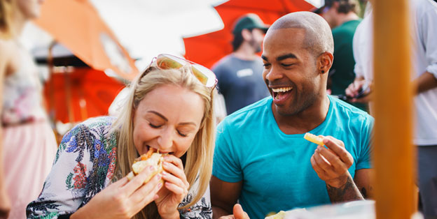 Couple eating hamburgers and French fries at outdoor picnic BBQ