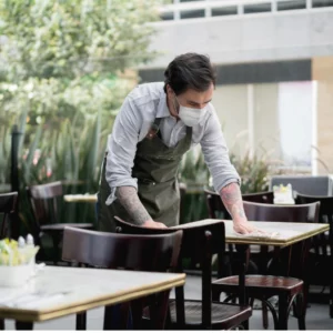 Restaurant Waiter wearing a facemask and cleaning table+